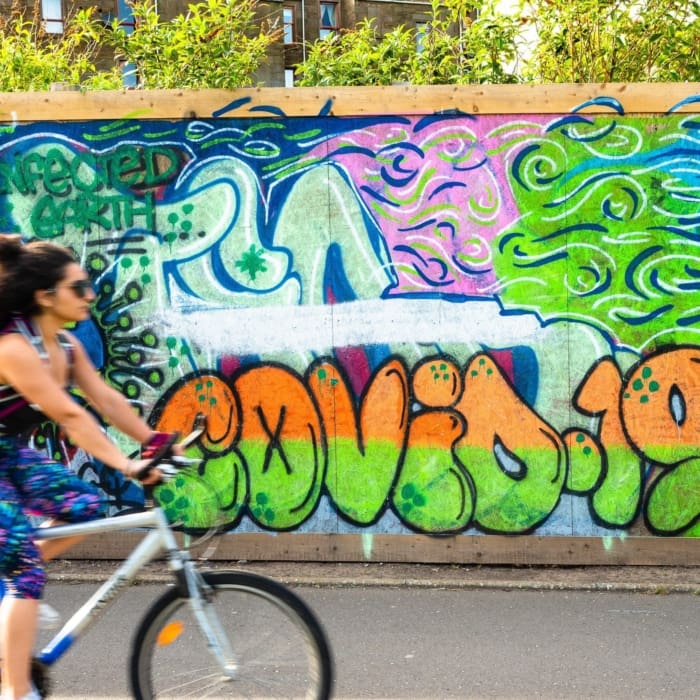 Cyclist passing COVID-19 graffitti in Dundee, Scotland. DD065